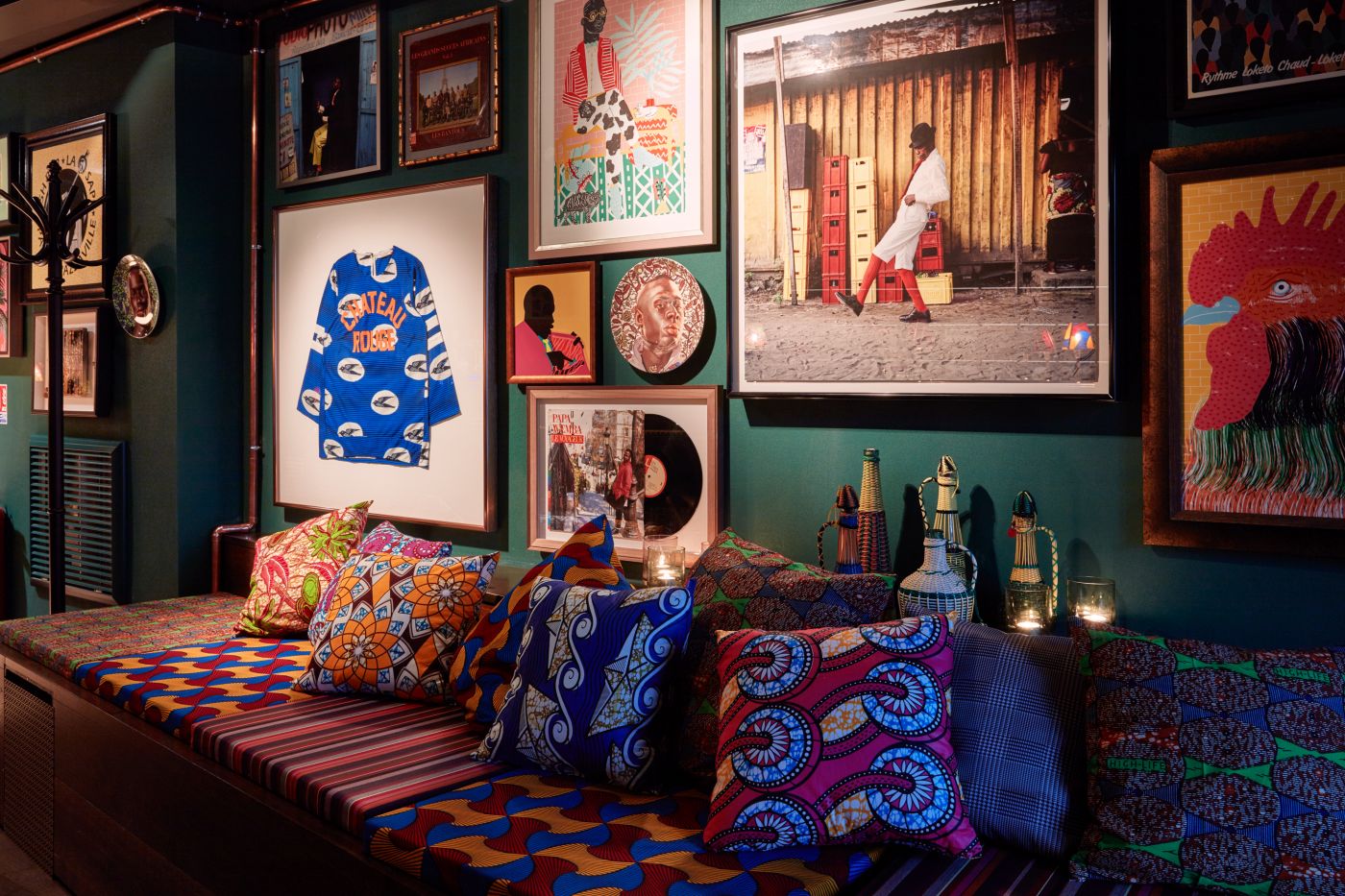 A wooden bench with colourful patterned cushions and pillows, the wall is filled with different artworks